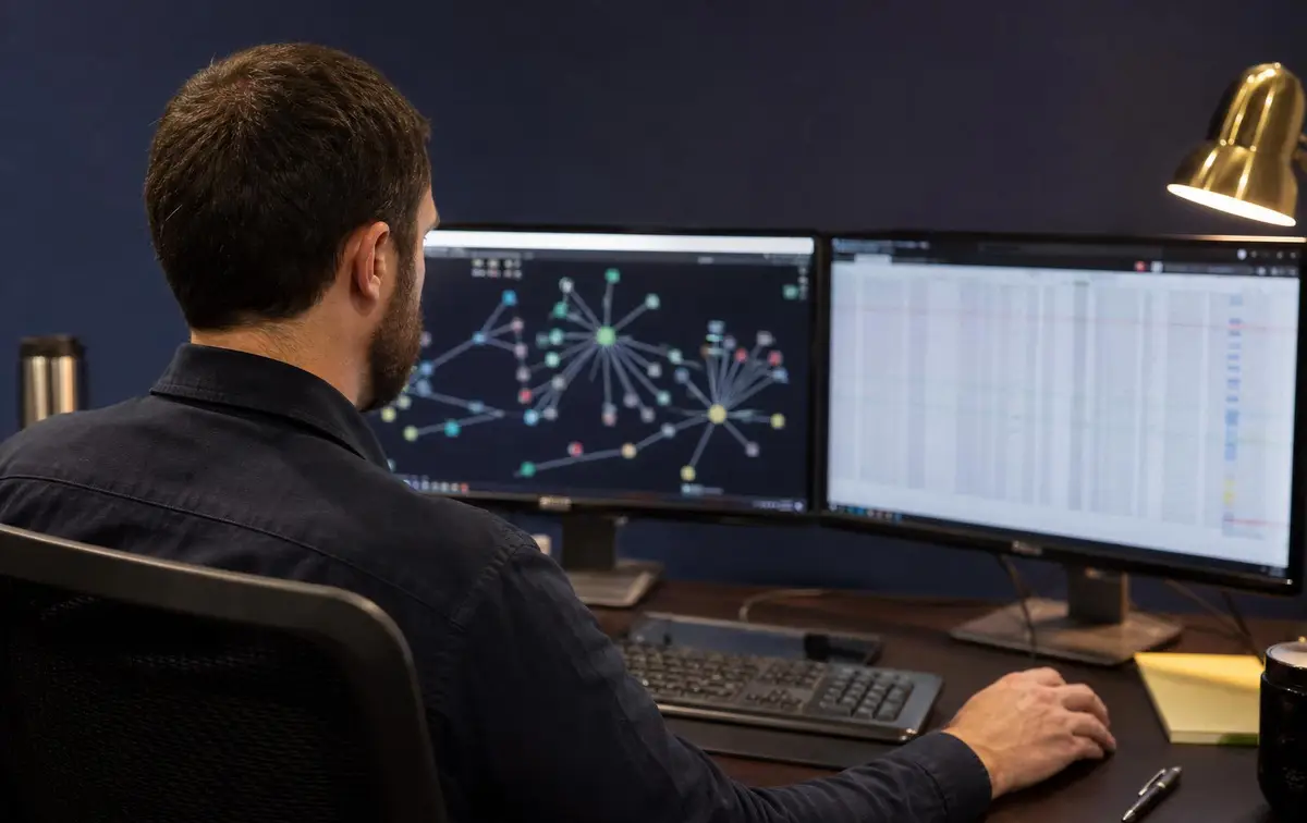Forensic analyst tracing cryptocurrency transactions across wallets, mixers and exchanges on multi-monitor blockchain forensics workstation
